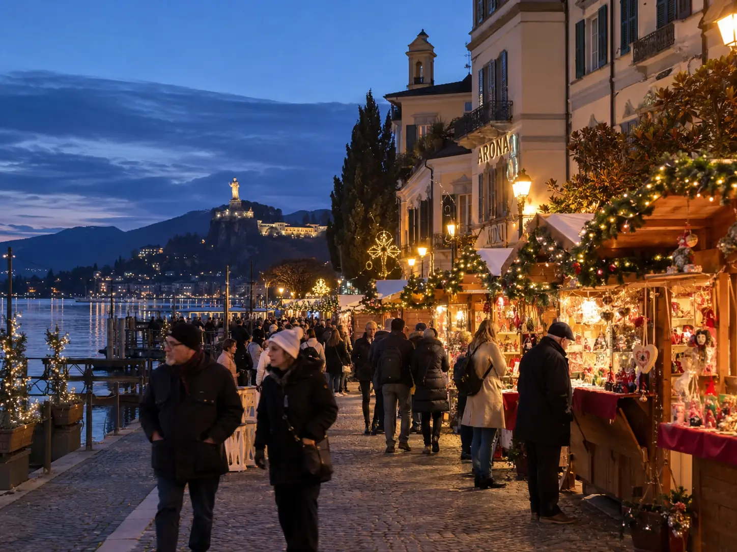Casette di Natale lungo il lungolago di Arona al tramonto, con la statua del San Carlone illuminata sulla collina