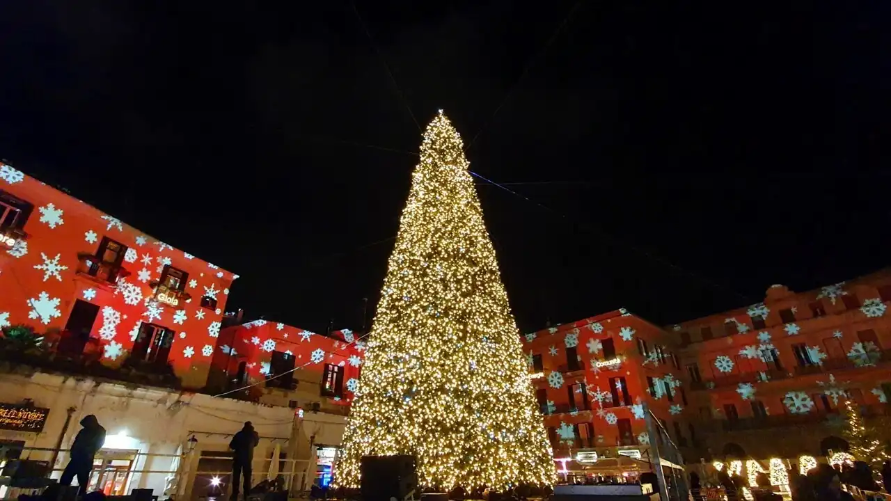Grande albero di Natale luminoso in una piazza con palazzi illuminati da proiezioni rosse a fiocchi di neve - mercatini di Natale di Bari