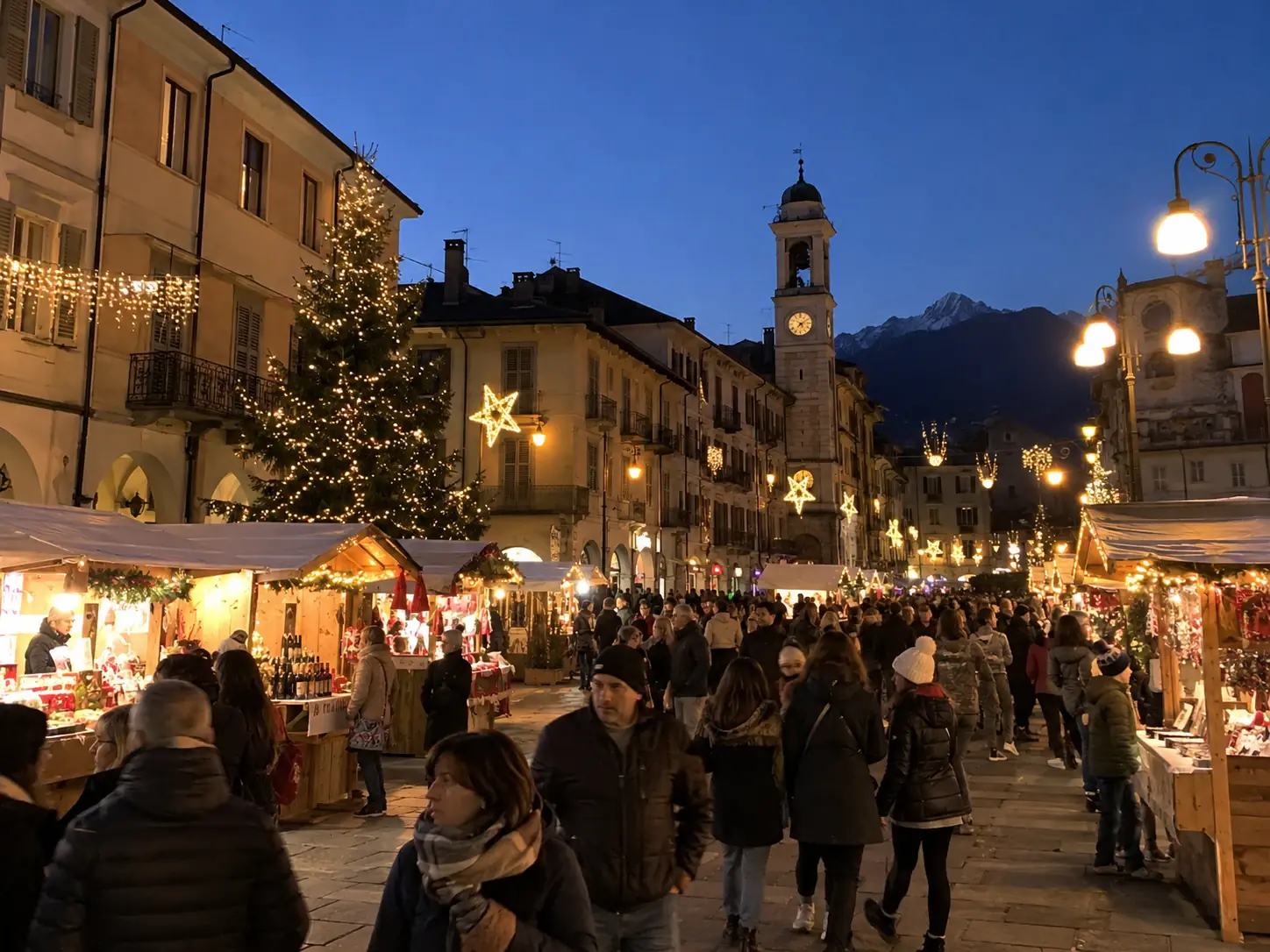 Mercatino di Natale in una via del centro di Cuorgnè con albero illuminato, stelle luminose, campanile e montagne sullo sfondo