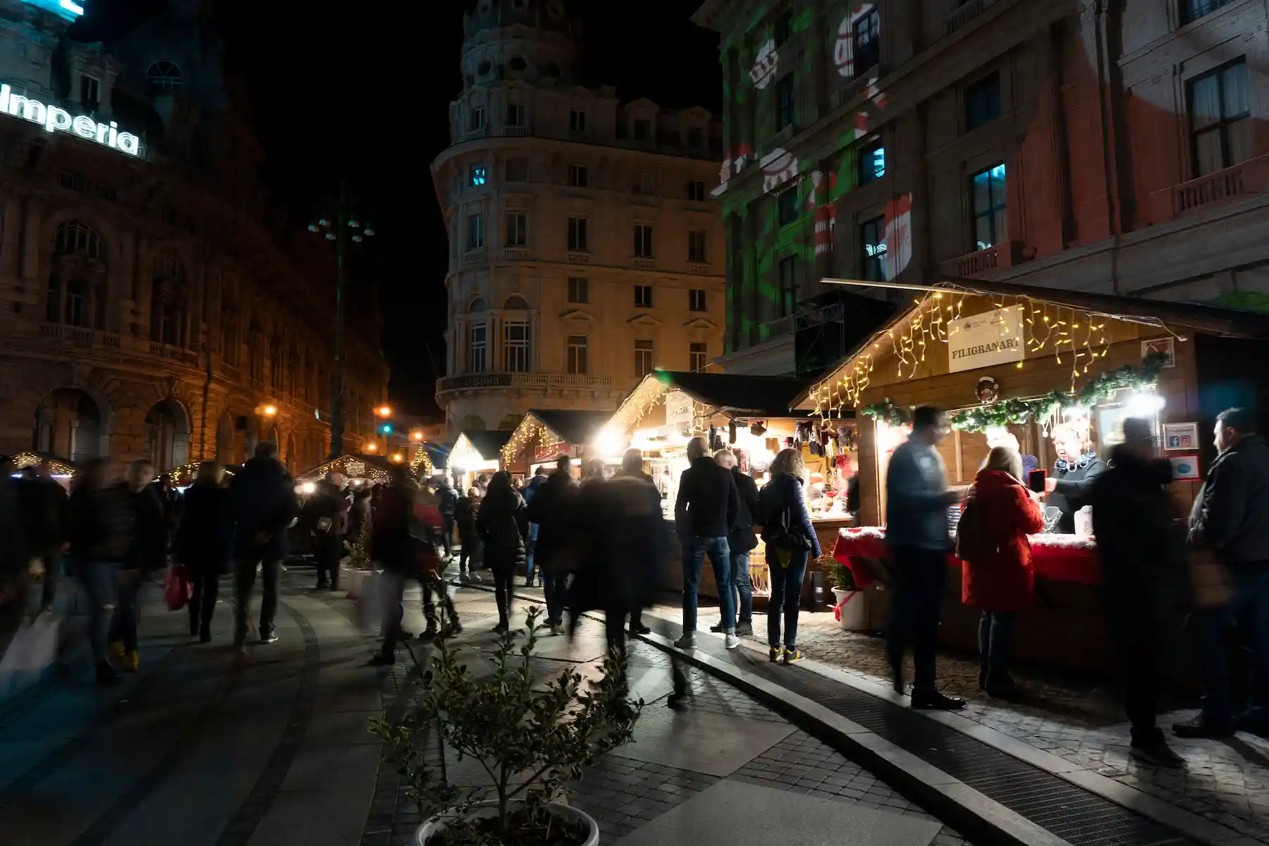Bancarelle del mercatino lungo una via del centro di notte, tra palazzi e passanti - mercatini di Natale di Genova