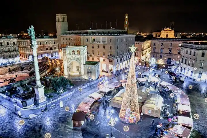 Piazza Sant'Oronzo a Lecce di sera vista dall'alto, con la colonna del santo, l'anfiteatro romano, il grande albero luminoso e le casette del mercatino