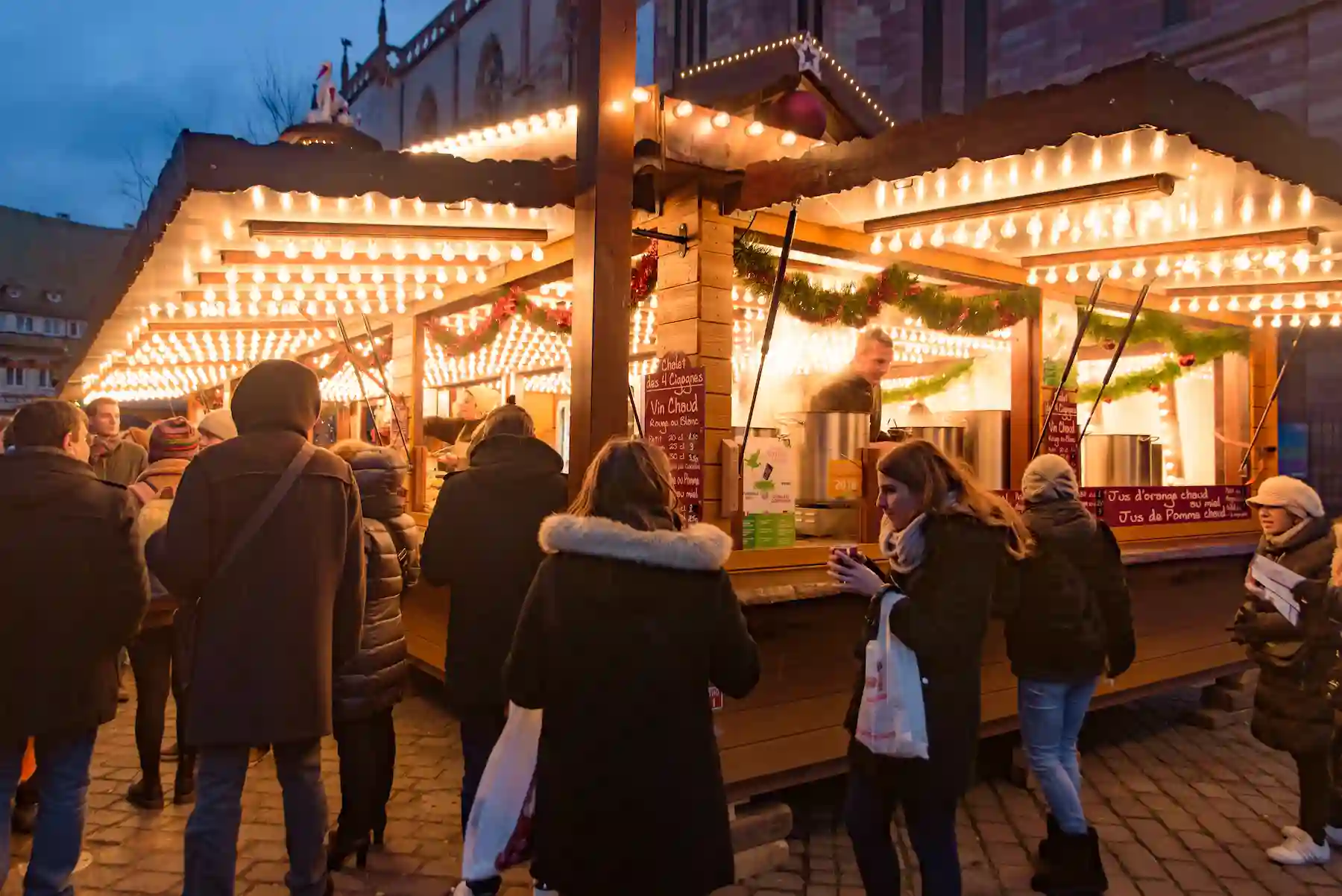 Casetta illuminata da luci calde con visitatori che passeggiano tra le bancarelle - mercatini di Natale di Mombaroccio