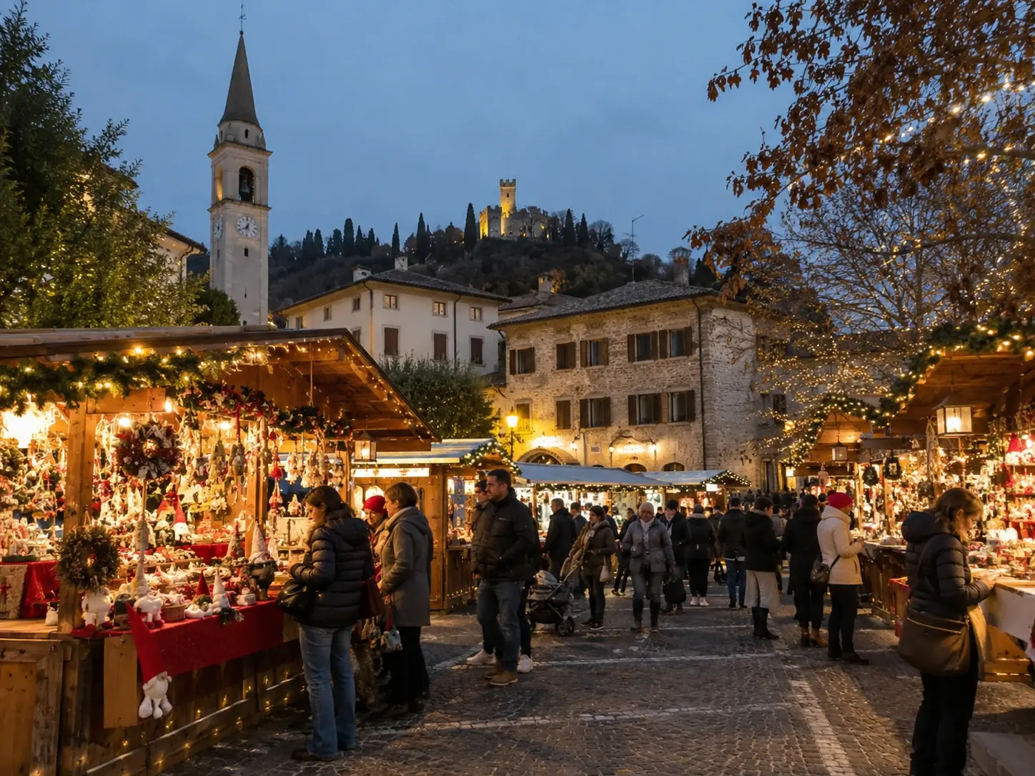 Bancarelle di Natale in una piazza del borgo con campanile e castello illuminato sulla collina, mercatini di Natale di Susegana e Collalto