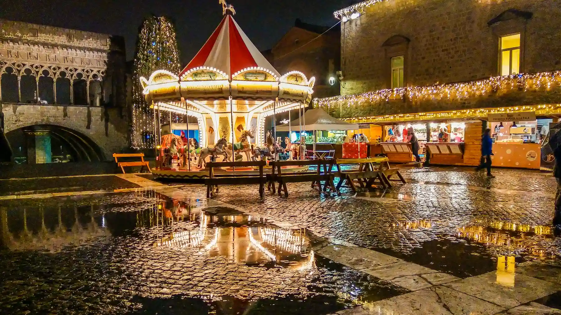 Giostra a carosello illuminata in una piazza lastricata e bagnata, di notte - mercatini di Natale di Viterbo