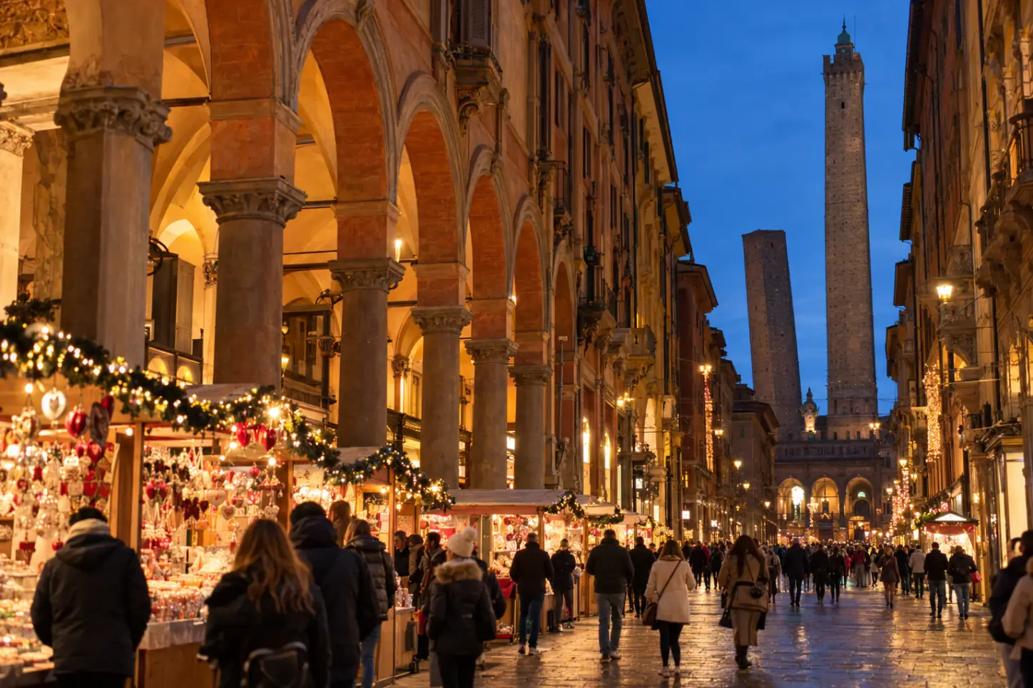 I portici di Bologna a Natale, con le bancarelle della fiera sotto le arcate e le Due Torri sullo sfondo, di sera