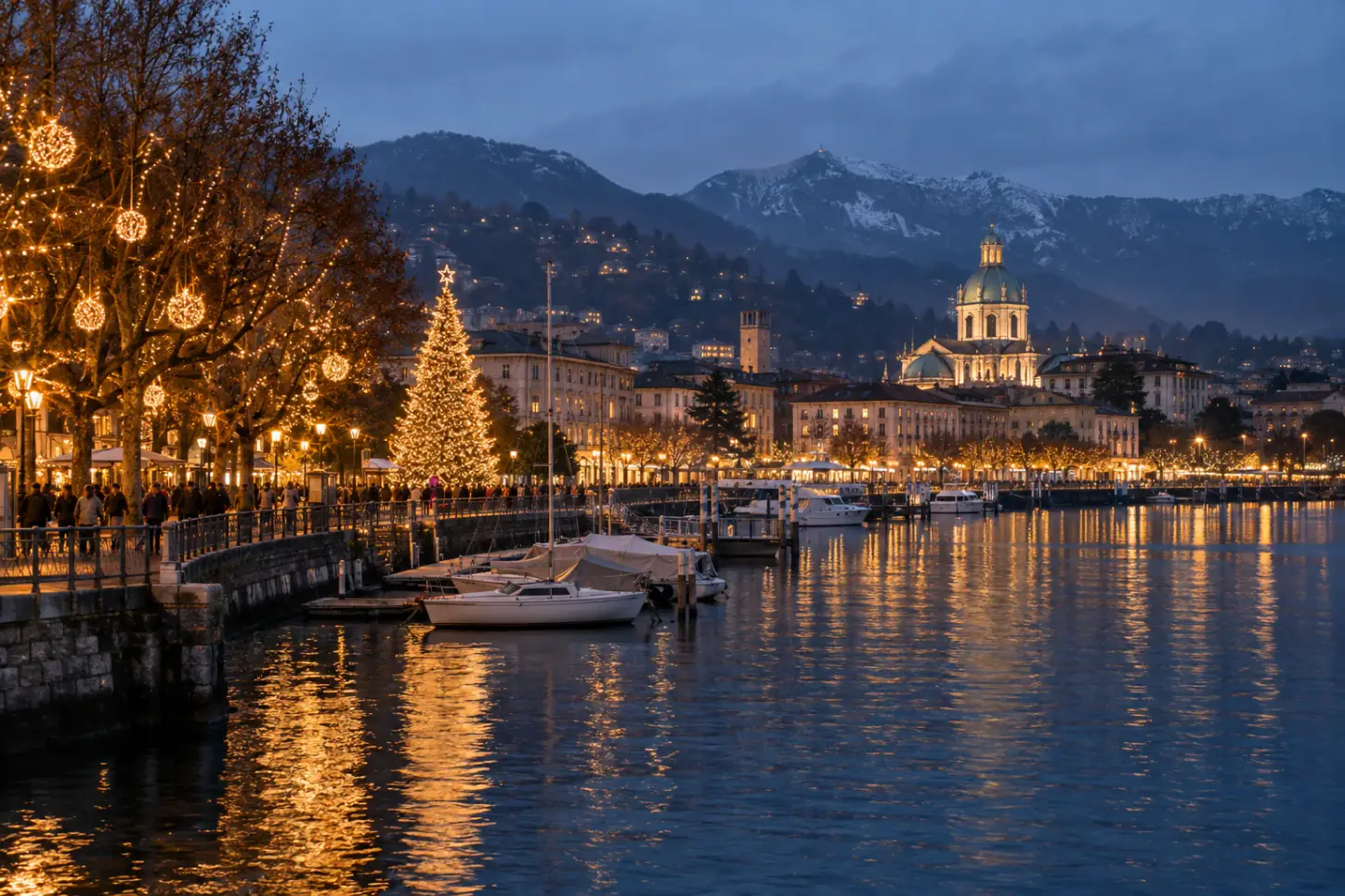 Il lungolago di Como a Natale al crepuscolo, con il grande albero illuminato, le luminarie e le montagne del lago sullo sfondo