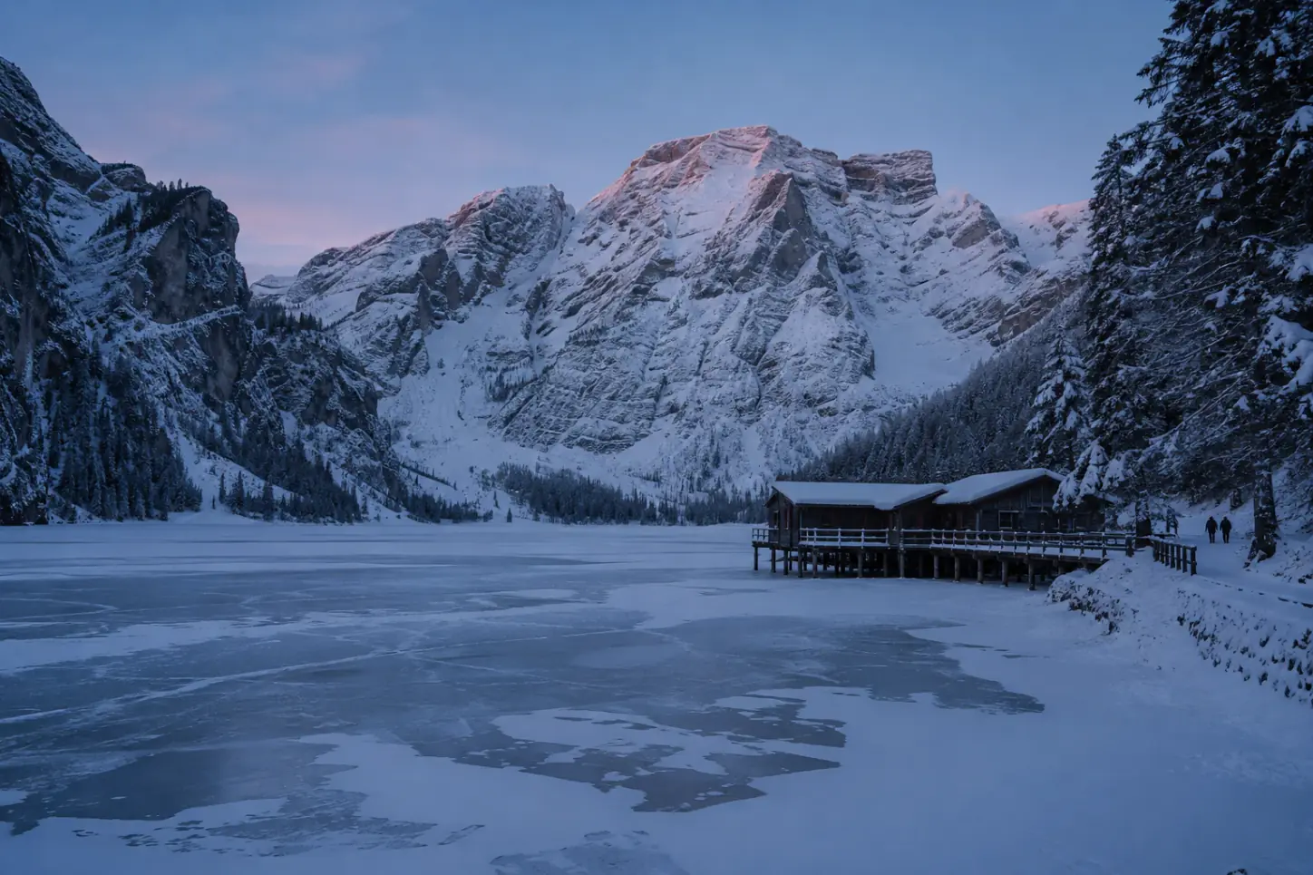 Il Lago di Braies ghiacciato in inverno con la storica rimessa in legno innevata e la parete rocciosa delle Dolomiti sullo sfondo