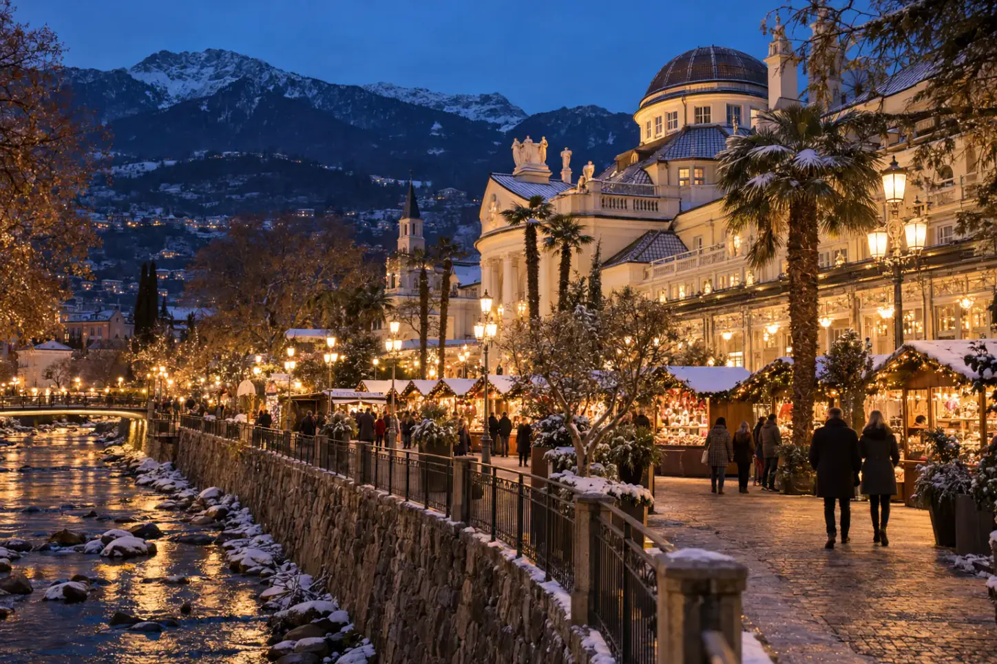 Mercatino di Natale di Merano lungo la passeggiata del Passirio, con il Kurhaus liberty illuminato, palme e montagne sullo sfondo