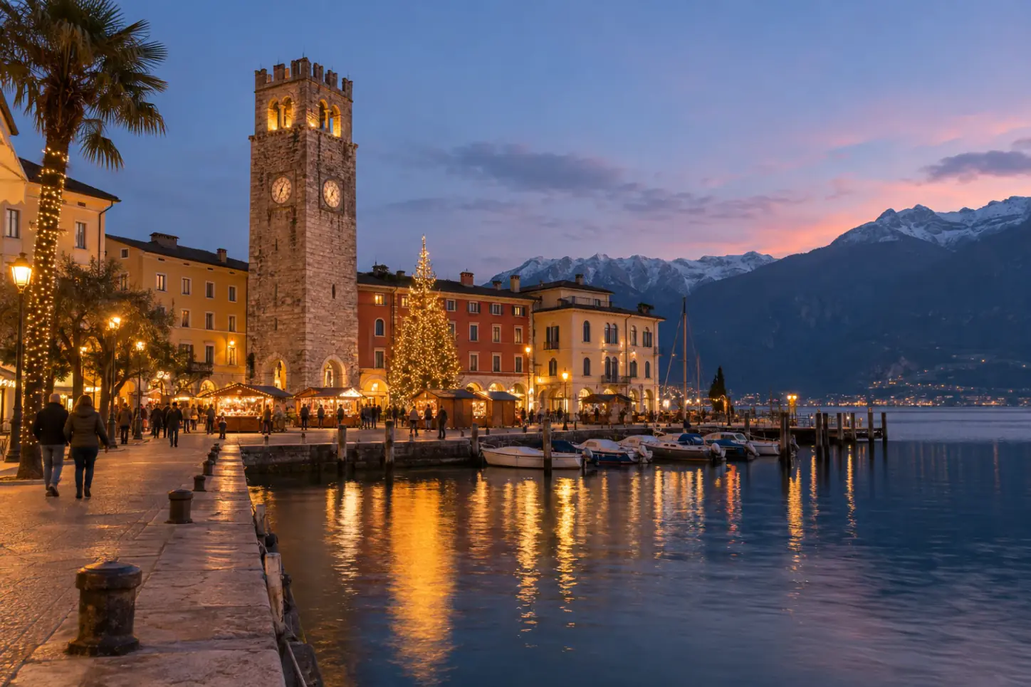 Riva del Garda a Natale con la Torre Apponale, le casette del mercatino in piazza e il Lago di Garda che riflette le luci